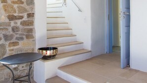 Una escalera que conduce a un segundo piso, un muro de piedra, una pequeña mesa con un cuenco y un techo de madera.