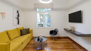 Una sala de estar moderna con un sofá amarillo, un sillón negro, una mesa redonda y un televisor en la pared.