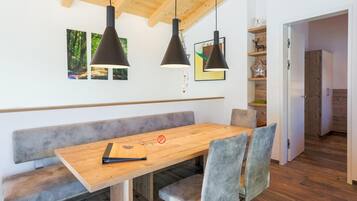 Un comedor moderno con una mesa de madera, sillas tapizadas en gris y lámparas colgantes negras.