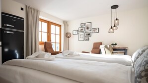 A hotel room with two beds, a desk, chairs, a refrigerator, and framed pictures on the wall. - Landhaus Lodges Kaprun - Franz (Kaprun)