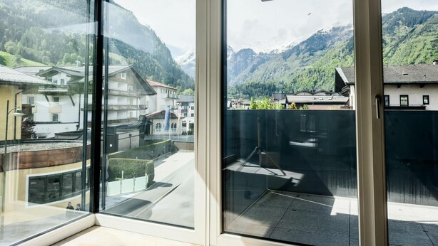 Un hotel moderno con amplios ventanales de piso a techo que ofrecen vistas a un paisaje montañoso y edificios tradicionales.
