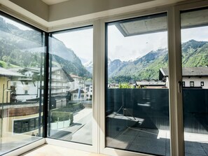 A modern hotel room with large floor-to-ceiling windows offering a view of a mountainous landscape and traditional buildings. - FP Appartements - Kitz 5 (Kaprun)