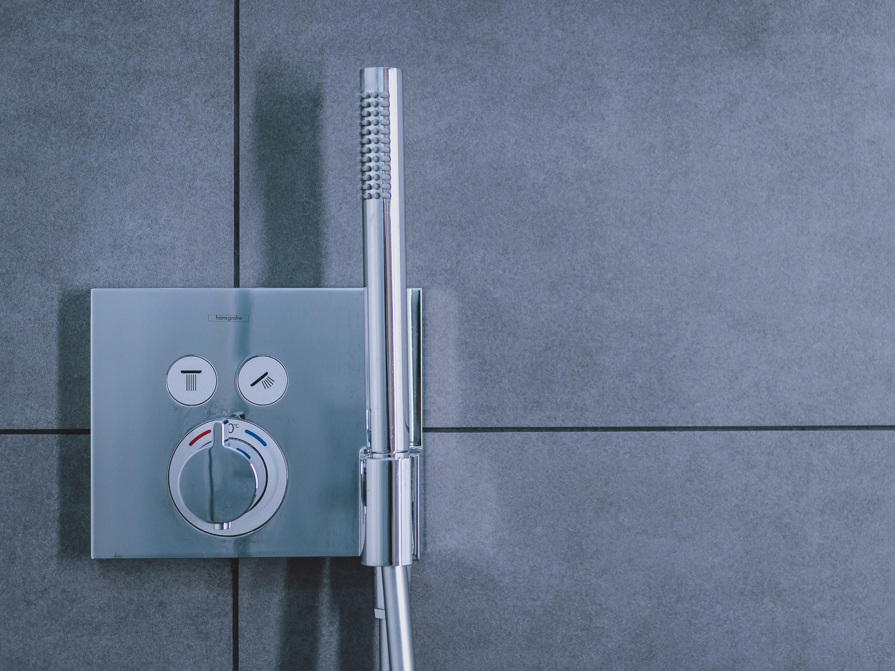A modern shower control panel with temperature and water flow settings, mounted on a tiled wall.