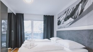 Habitación de hotel con dos camas, un ventanal con cortinas, vista a la montaña y un cuadro de montaña.