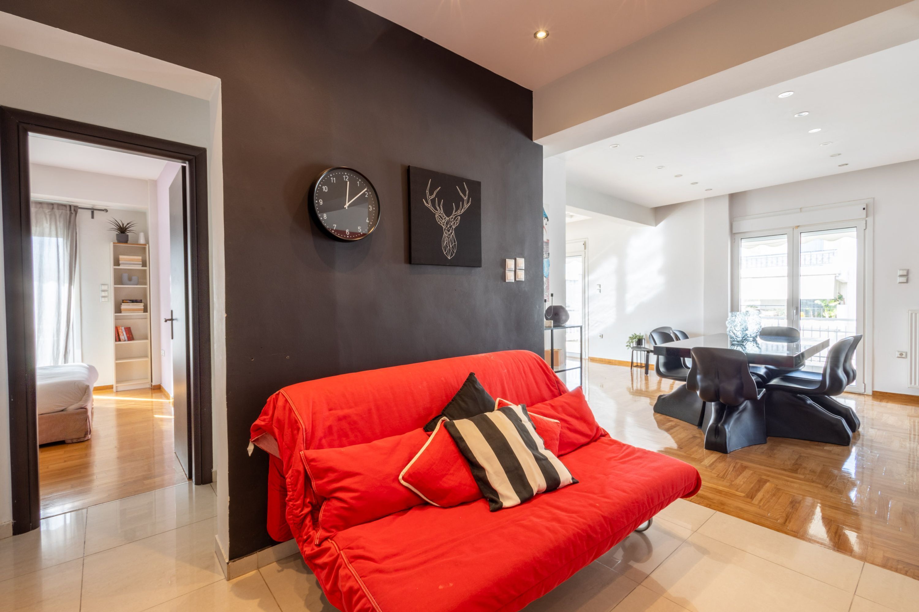 A modern living room with a red sofa, a black clock, and a deer head artwork on the wall.