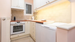 A compact kitchen with white cabinets, a built-in oven, a coffee maker, and a small refrigerator. - Thissio Cocoon For Two (Athens)