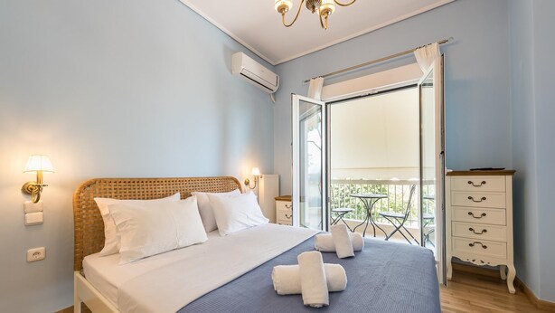 A bedroom with a bed, a nightstand, a dresser, a balcony with a table and chairs, and an air conditioning unit. - Thissio Cocoon For Two (Athens)