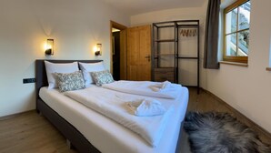 Uma cama bem arrumada com cabeceira, duas luminárias fixadas na parede e uma janela com cortinas.