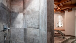 Um banheiro moderno com grandes azulejos de pedra, área de chuveiro e escada que leva a outro nível.
