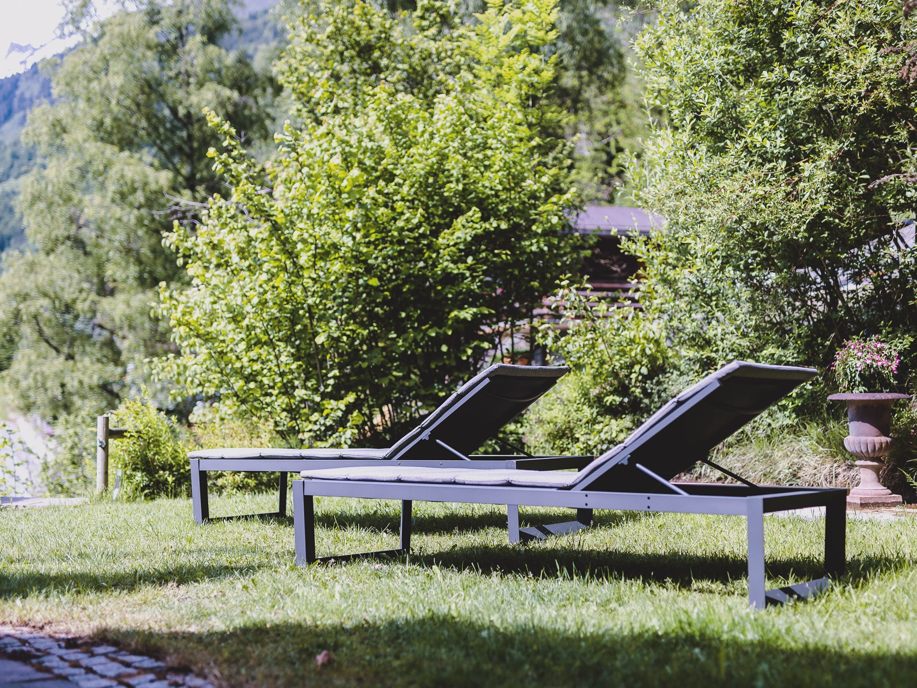 Two sun loungers in a grassy area with a tree and a building in the background.
