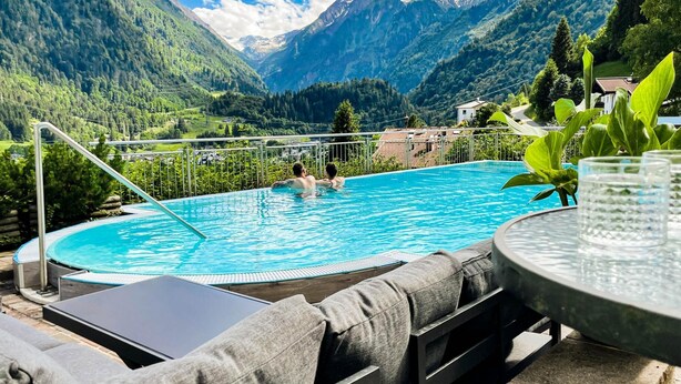 Piscina com duas pessoas, rodeada por montanhas e vegetação.