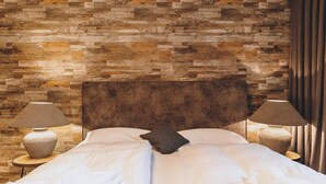 A bed with a wooden headboard, two bedside lamps, and a stone-patterned wall behind it. - Alpine City Living - TOP 21 (Zell am See)