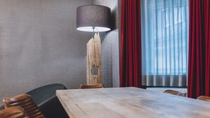 Une salle de conférence avec une table en bois, des chaises, une lampe et une fenêtre ornée de rideaux rouges.