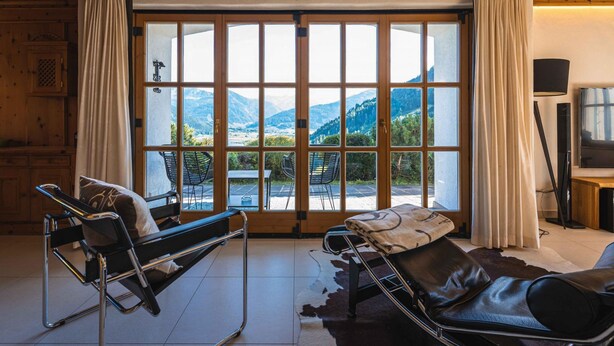 A room with a large sliding glass door leading to a mountain view, a bed, a chair, and a television. - Chalet Crown of the Alps (Zell am See)