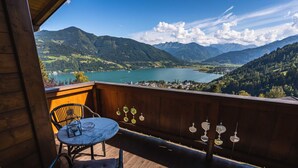 A wooden balcony with a round table and chairs, overlooking a lake and mountains. - Chalet Crown of the Alps (Zell am See)