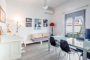 Quarto moderno com mesa de vidro, paredes brancas, sofá, luminária vermelha e quadros emoldurados.