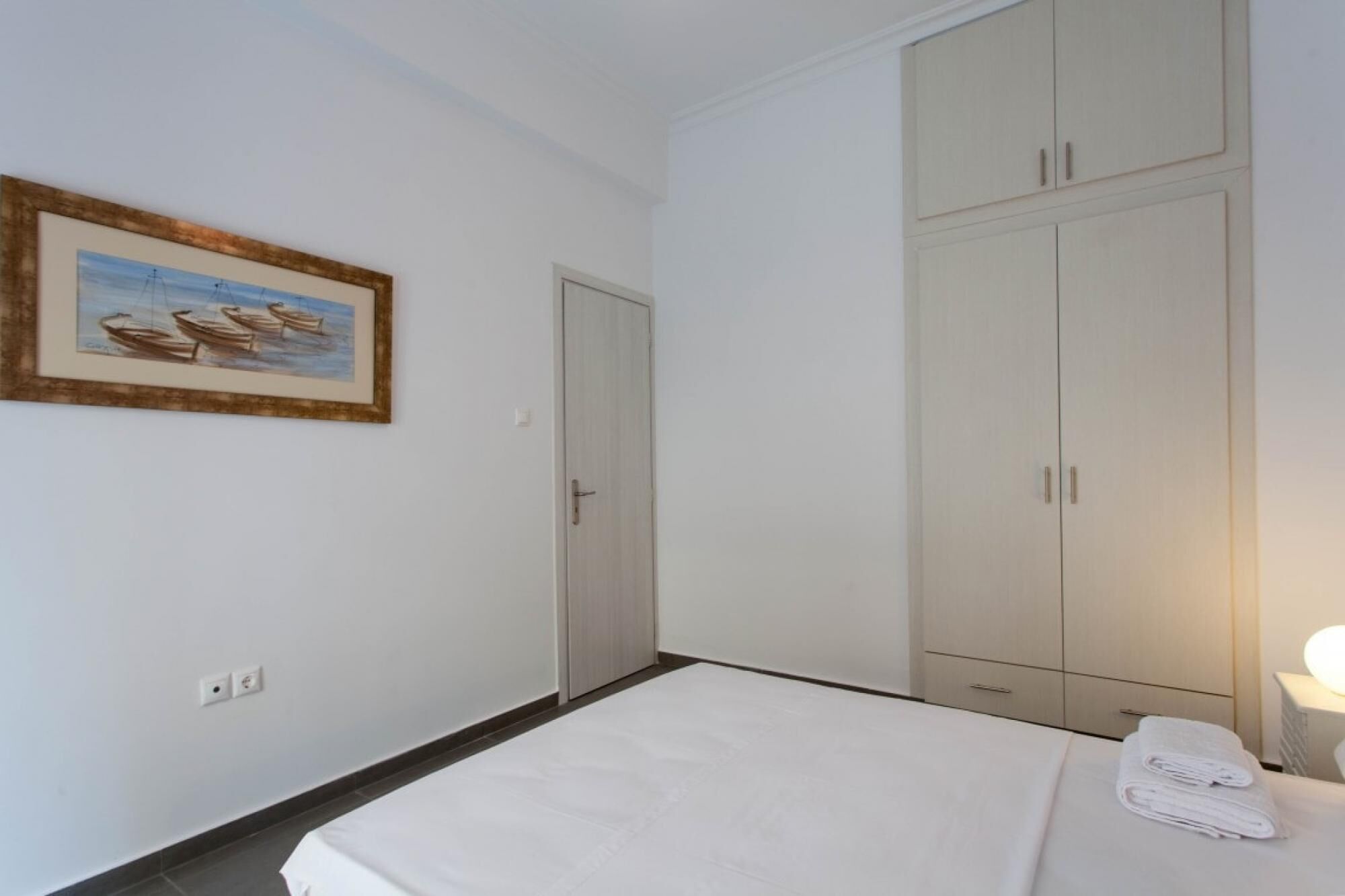 Una habitación de hotel con cama, armario, puerta y un cuadro en la pared.