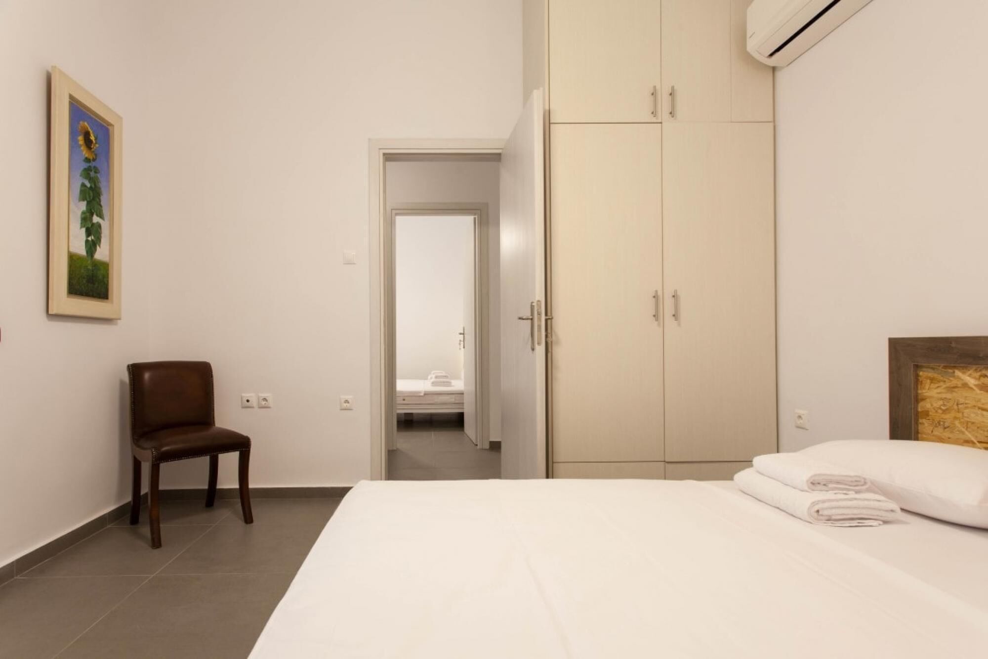Een hotelkamer met een bed, een stoel, een kledingkast en een deur naar een andere kamer.