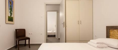 Een hotelkamer met een bed, een stoel, een kledingkast en een deur naar een andere kamer.
