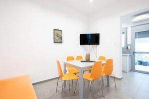 Uma sala de conferências com uma mesa de vidro, cadeiras laranja, uma TV de tela plana e um quadro na parede.