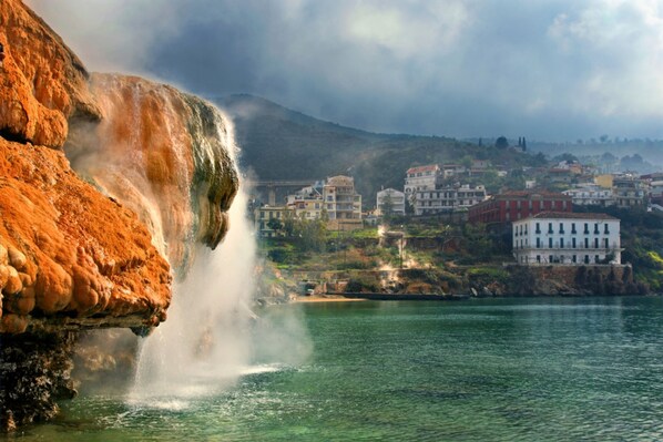 Una cascada que vessa en una massa d'aigua, amb edificis al fons.