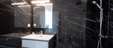 Un baño moderno con piso de mármol, lavamanos blanco, un espejo grande y una ducha con múltiples cabezales.