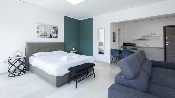 A modern bedroom with a bed, bedside table, bench, and a grey sofa. - Hip And Fun in Athens Apt B (Athens)