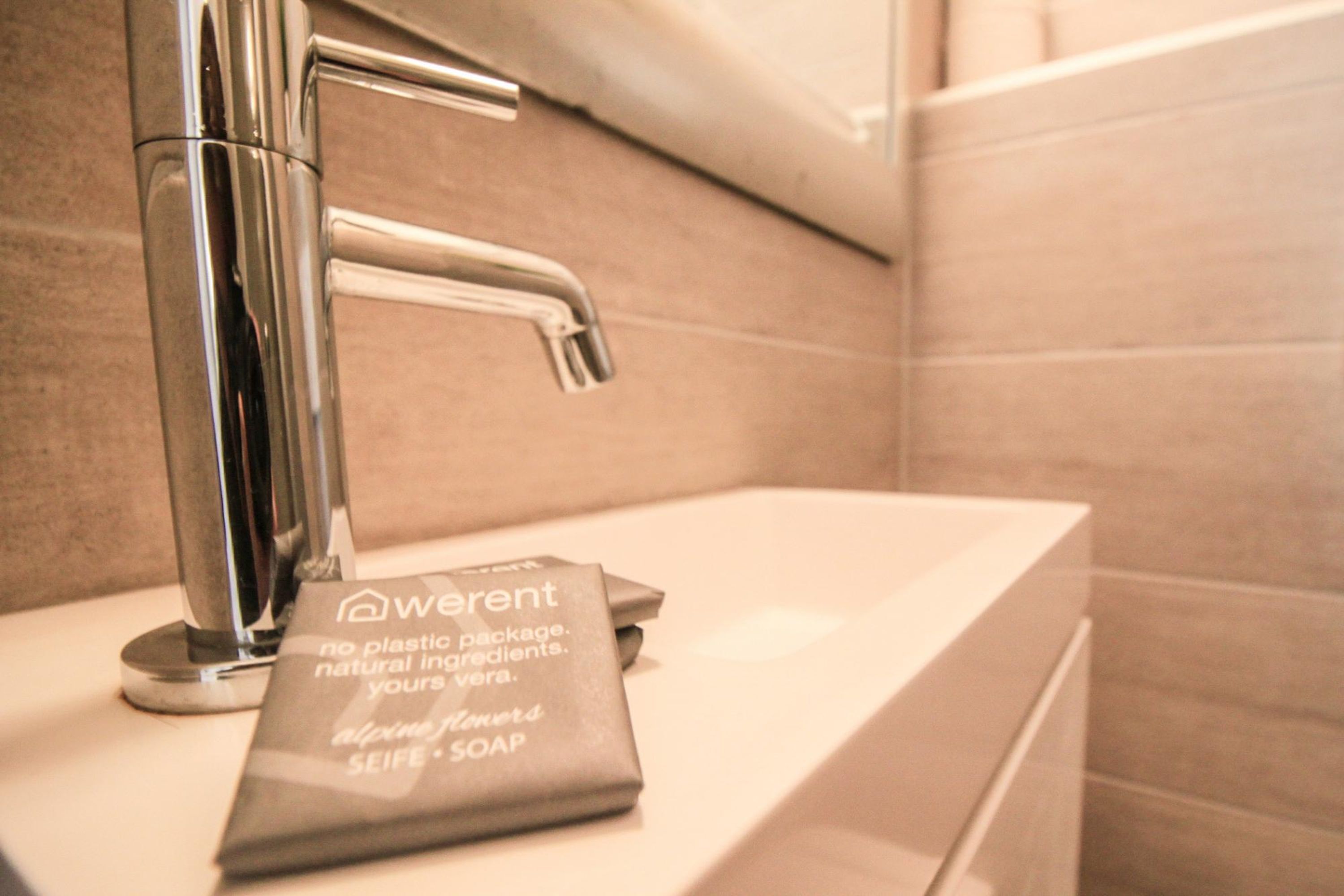 A bathroom sink with a chrome faucet and a soap dispenser labeled "Alpine Flowers SEIFE - SOAP."