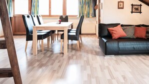 Ein Wohnzimmer mit schwarzem Ledersofa, Esstisch aus Holz und Stühlen.