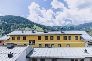 Un bâtiment jaune, doté de nombreuses fenêtres et d’un toit plat, entouré de collines verdoyantes et surplombant un ciel dégagé.