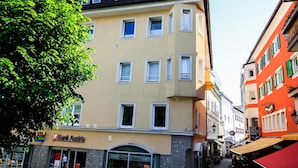 A multi-story building with a 'Bank Austria' sign, a tree in front, and a narrow street with shops. - Alpine City Living - TOP 31 (Zell am See)