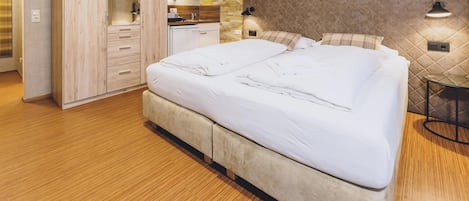 A bedroom with a bed, wooden wardrobe, and a small kitchenette.