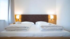 A double bed with white linens, two bedside tables with towels, and wall-mounted lamps. - Lake View Suites Villa Julia - Terrace Suite (Zell am See)