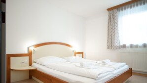 A neatly made double bed with white linens, a wooden headboard, and a bedside table with a lamp. - Seilergasse Apartments - TOP 6 (Zell am See)