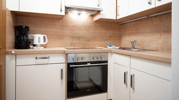 A compact kitchen with a built-in oven, a coffee maker, and a sink. - Seilergasse Apartments - TOP 6 (Zell am See)