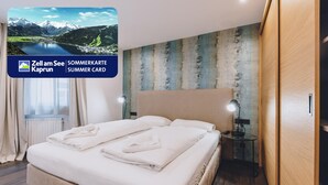 Een hotelkamer met een bed, een nachtkastje, een lamp en uitzicht op een bergmeer.