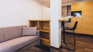 Een moderne woonkamer met een bank en een kleine tafel, een kitchenette met houten keukenkastjes, en een barkruk.
