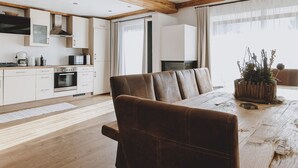 A modern kitchen with wooden beams, white cabinetry, and a dining area with a wooden table and leather chairs. - Chalet Molly in Zell am See (Zell am See)