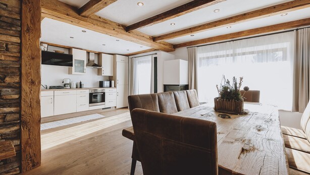 A spacious dining area with a wooden table and leather chairs, a kitchen in the background, and a stone wall on one side. - Chalet Molly in Zell am See (Zell am See)