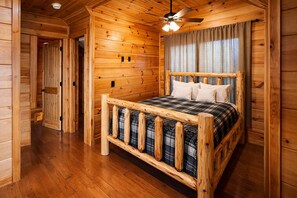A wooden cabin bedroom with a bed, a ceiling fan, and a window with curtains. - Private Large Mountaintop Cabin w/ wraparound deck (Dobson)