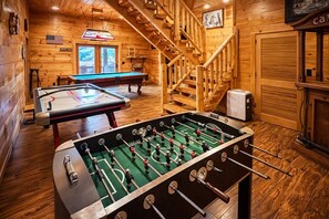 Una habitación con piso de madera, una mesa de fútbol de mesa y una mesa de billar, además de una escalera.