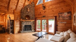 L’intérieur d’une cabane en rondins, avec une cheminée en pierre, des murs en bois, une table à manger et un canapé.