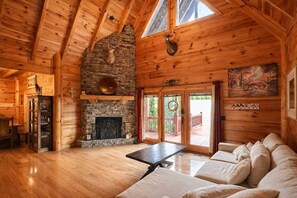 A log cabin interior with a stone fireplace, wooden walls, a dining table, and a sofa. - Private Large Mountaintop Cabin w/ wraparound deck (Dobson)