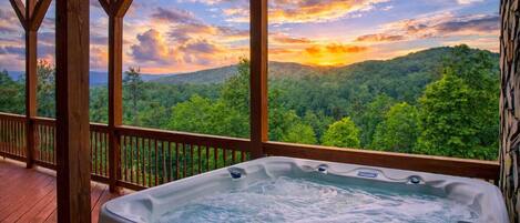 Een hottub op een houten terras, met uitzicht op een bebost berglandschap.