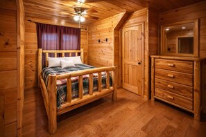 Una habitación de cabaña de madera con una cama, un tocador y un ventilador de techo.