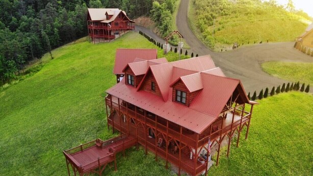 Une grande cabane en bois rouge, dotée d’un porche et d’un coin repas, entourée d’une pelouse bien entretenue et d’arbres.