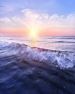 Een zonsondergang boven de oceaan, met golven die de kust naderen.