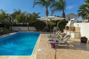 Relax by the serene pool surrounded by lush greenery and lounge chairs.
