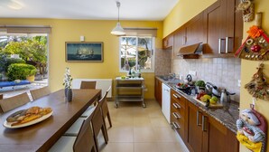 Een moderne keuken met houten kastjes, een eettafel met stoelen, een klein eiland met een spoelbak en uitzicht op de omgeving.