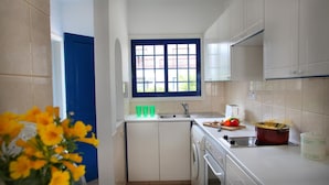 A compact kitchen with white cabinets, a blue-framed window, a sink, and a stove. - Villa Julie in Protaras (Paralimni)